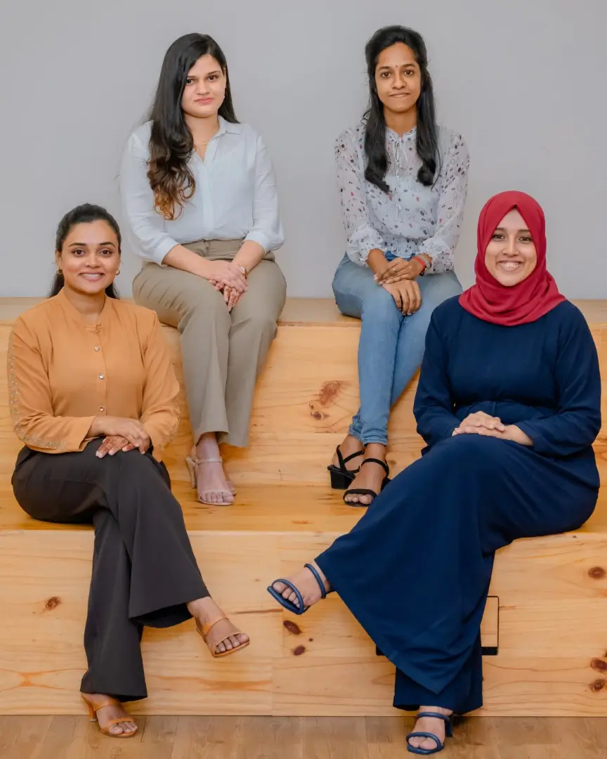 Four smiling women posing indoors.